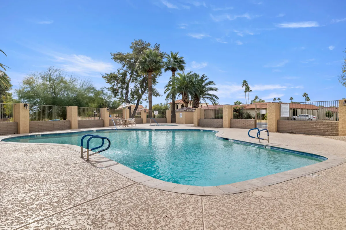 The hero image captures the inviting backyard of the Andravida, featuring a sparkling swimming pool surrounded by swaying palm trees and plush lounge chairs. The sun sets in the background, casting a warm, golden glow over the scene, while the poolside area is perfectly arranged for both quiet relaxation and joyful gatherings.