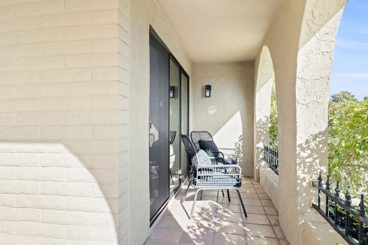 A tranquil exterior patio setting with chairs, railings, and lush potted plants. The space is designed for relaxation, with views that suggest a peaceful outdoor experience suitable for enjoying coffee while overlooking a greenbelt area.