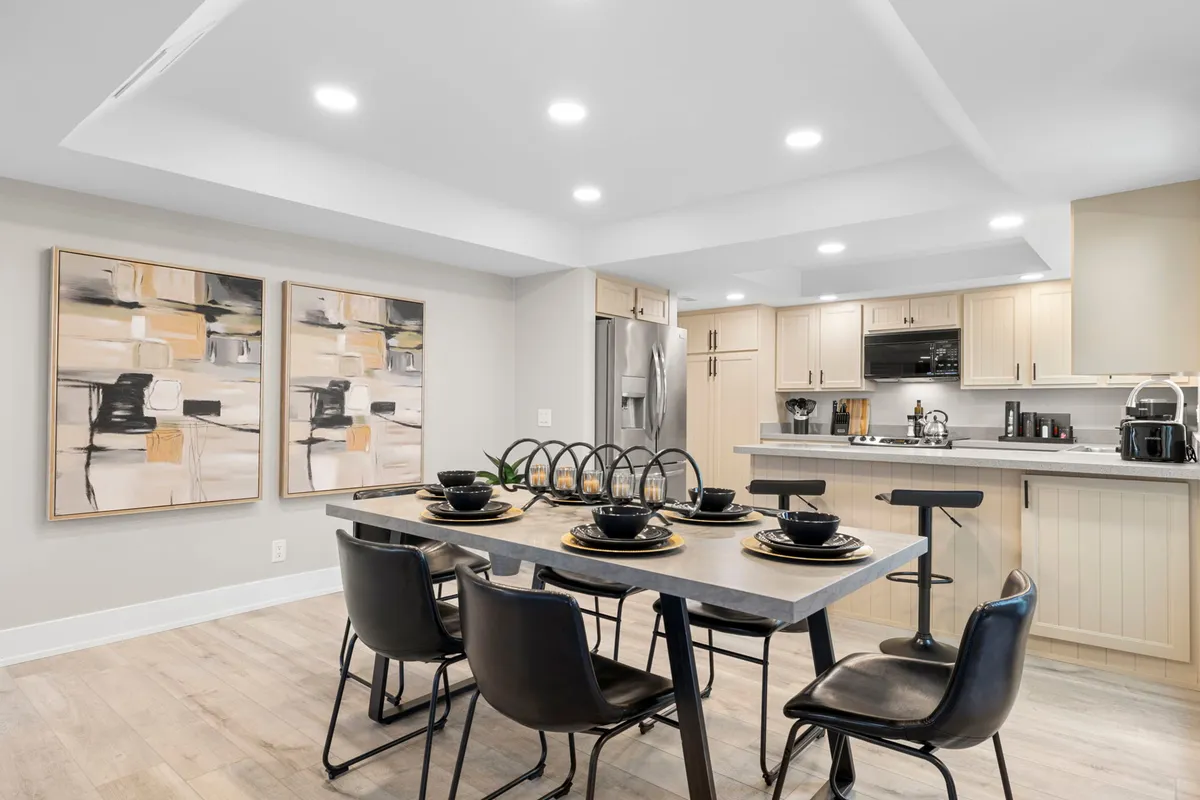 A close-up of the dining table set with black plates, flanked by stylish chairs, with the kitchen area visible in the background. Modern abstract art graces the wall, and the kitchen’s clean lines and ample light suggest a welcoming spot for both formal dinners and casual meals.