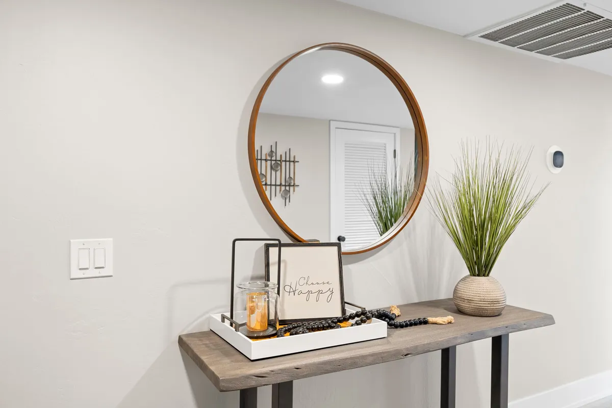 A stylish, welcoming interior scene featuring a wooden table decked with a decorative tray, a round mirror reflecting light, and touches of greenery. The space feels inviting and modern, suggesting a calm entry point that sets the tone for both relaxation and productivity.