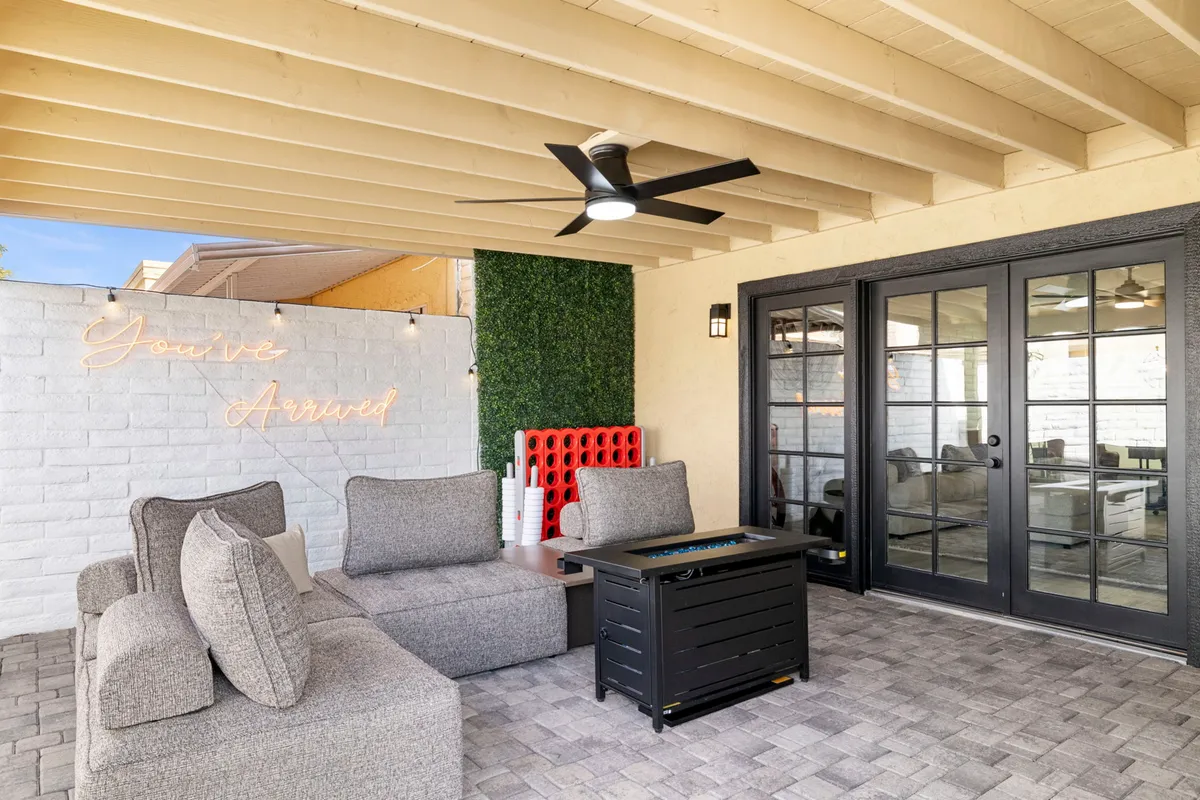 A stylish lounge area with comfortable sofa seating, a neon sign reading 'You've Arrived,' a black door leading to the interior, and an artificial green wall. The setup feels contemporary and welcoming, ideal for gatherings and evening relaxation.