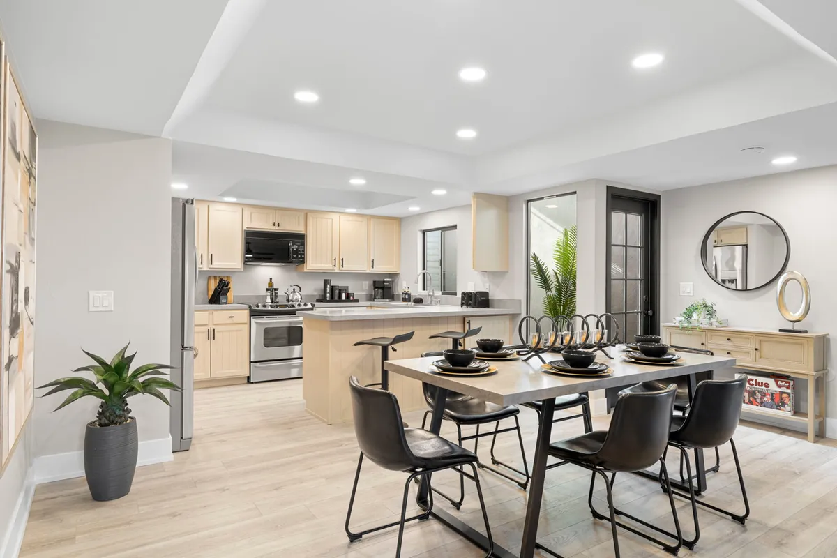 An inviting open-plan space featuring a dining table, kitchen island, decorative artwork, and a potted plant. The room feels lively and perfect for family get-togethers, with clear zones for preparing, serving, and enjoying meals.